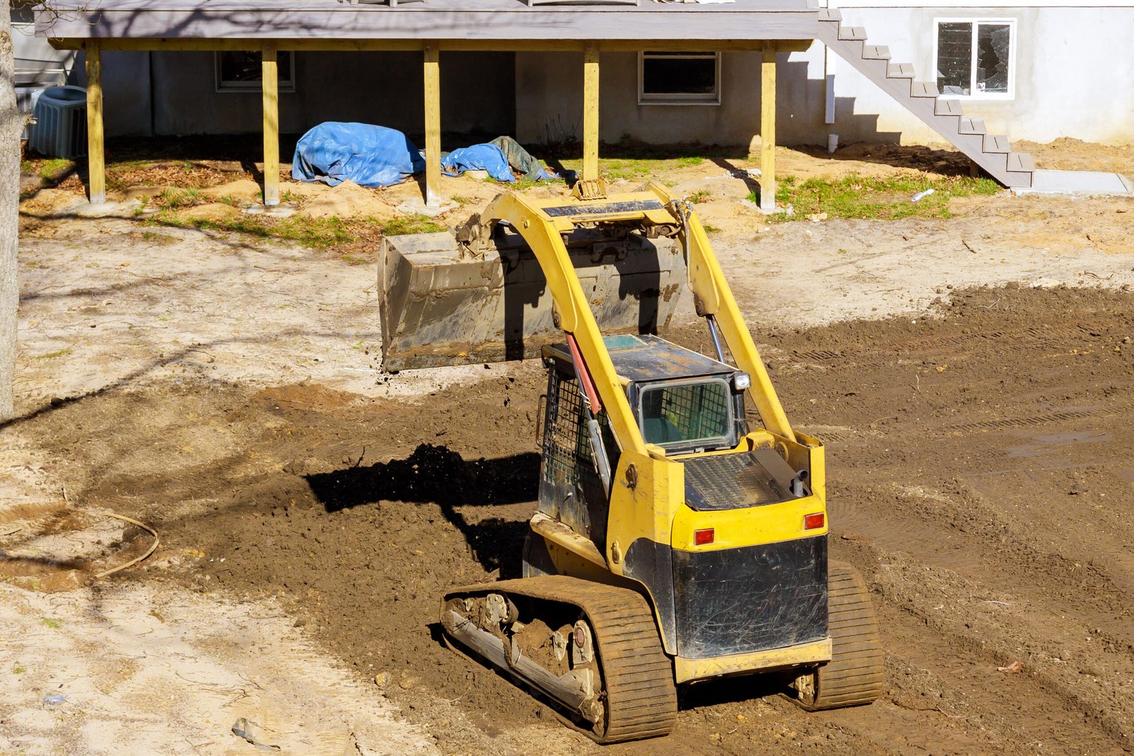 An earthmoving tractor is leveling ground at a construction site for cleaning backyard An earthmoving tractor is leveling ground at construction site for cleaning backyard