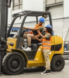 Engineers using a digital tablet while driving a forklift in a factory
